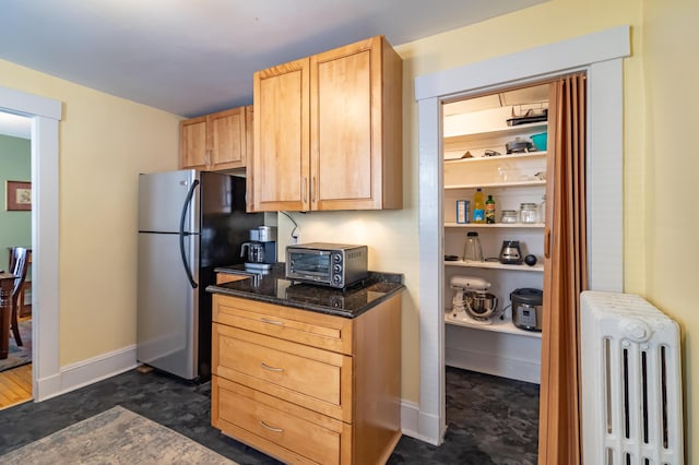 kitchen with dark stone countertops, radiator, stainless steel fridge, and light brown cabinets