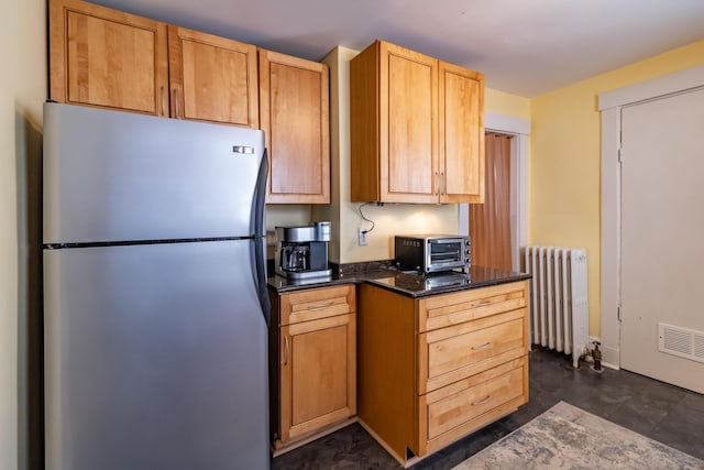 kitchen with light brown cabinets, radiator, dark stone countertops, and stainless steel refrigerator