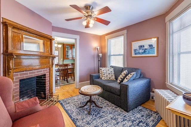 living room featuring radiator, a fireplace, ceiling fan, and light wood-type flooring