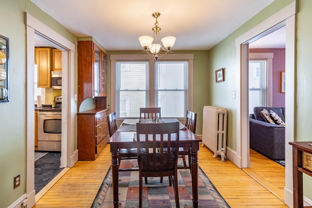 dining space with radiator heating unit, light hardwood / wood-style floors, and a notable chandelier