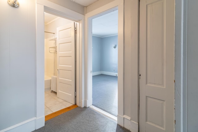 corridor with crown molding, radiator, and light carpet