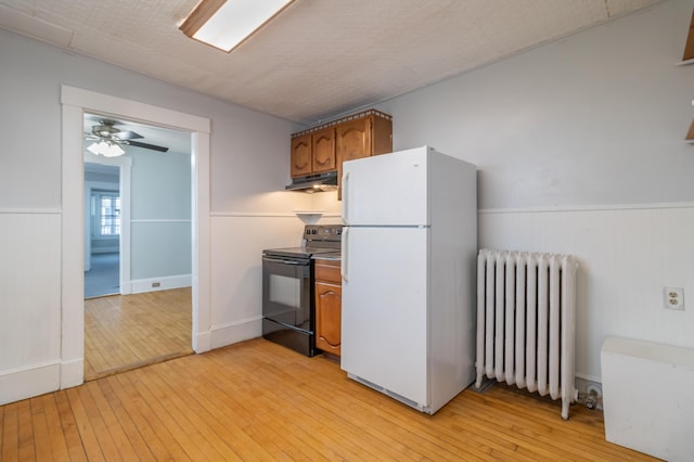 kitchen featuring black electric range oven, light wood-type flooring, radiator, white fridge, and ceiling fan