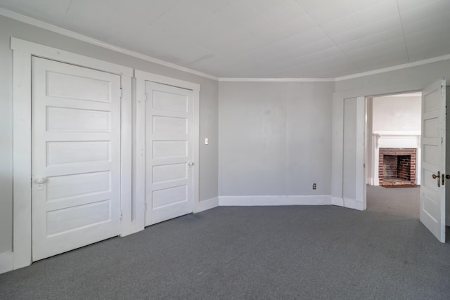 unfurnished bedroom with dark colored carpet, a brick fireplace, and crown molding