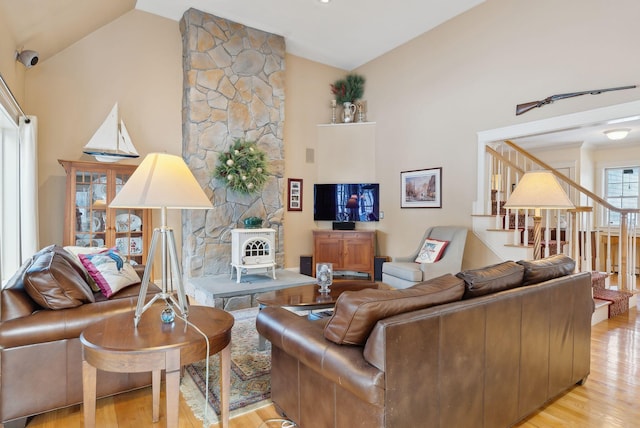 living room with high vaulted ceiling, a wood stove, and light hardwood / wood-style floors