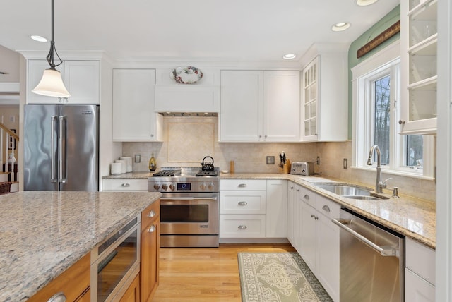 kitchen with white cabinetry, sink, premium appliances, hanging light fixtures, and light stone counters