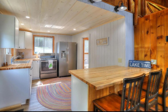 kitchen featuring stainless steel appliances, a breakfast bar, wooden counters, and white cabinetry