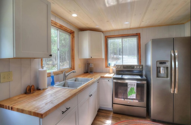 kitchen with stainless steel appliances, a sink, wood counters, and white cabinets