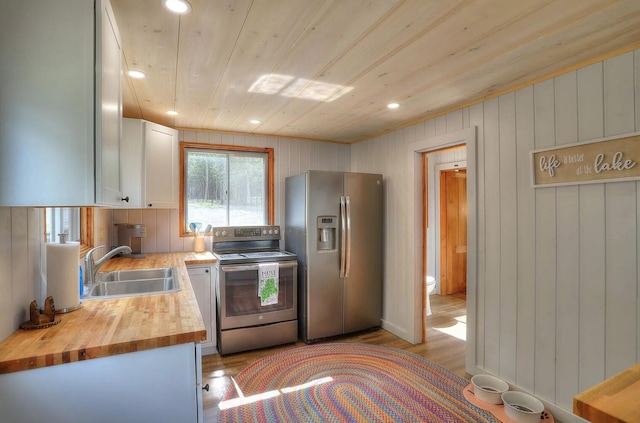 kitchen with stainless steel appliances, white cabinetry, a sink, butcher block countertops, and light wood-type flooring