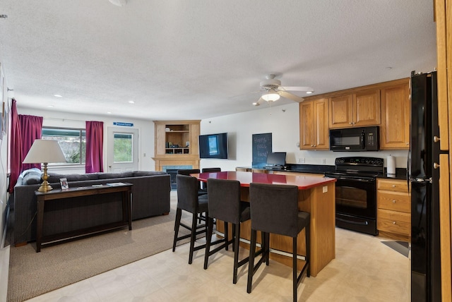 kitchen with a large fireplace, a kitchen breakfast bar, a center island, black appliances, and a textured ceiling