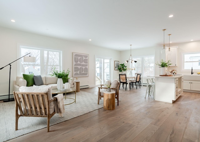 living room with sink, baseboard heating, and light hardwood / wood-style flooring