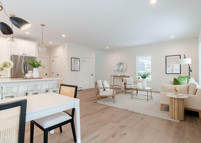 interior space with white cabinets, hanging light fixtures, stainless steel fridge, and light wood-type flooring