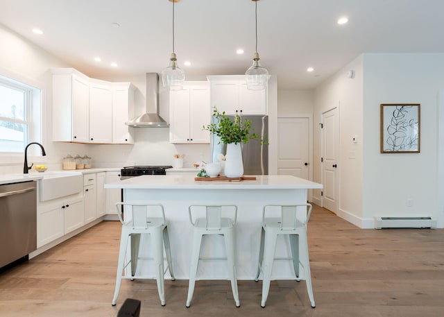 kitchen featuring a kitchen island, appliances with stainless steel finishes, a baseboard radiator, white cabinets, and wall chimney exhaust hood