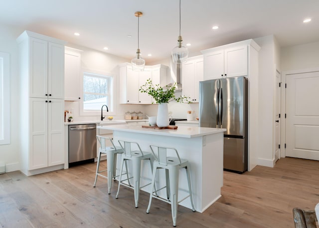 kitchen featuring appliances with stainless steel finishes, white cabinetry, a center island, decorative light fixtures, and wall chimney exhaust hood