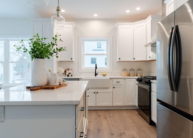 kitchen with pendant lighting, sink, stainless steel fridge, black gas stove, and white cabinets