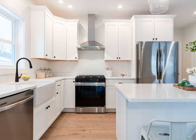 kitchen with white cabinetry, stainless steel appliances, light hardwood / wood-style flooring, and wall chimney range hood