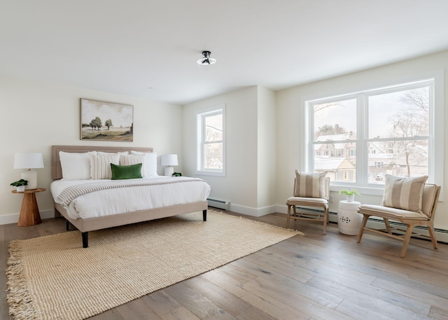 bedroom with baseboard heating, light hardwood / wood-style floors, and multiple windows