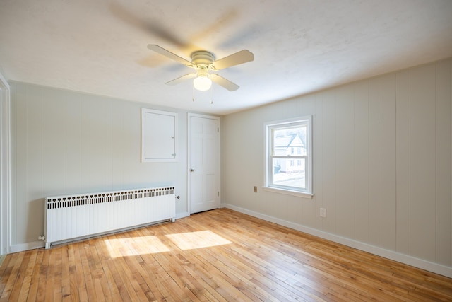 unfurnished room with light wood-type flooring, radiator, ceiling fan, and baseboards