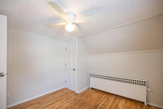 bonus room with baseboards, radiator heating unit, ceiling fan, a textured ceiling, and light wood-style floors