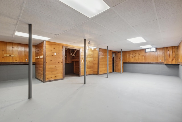 basement featuring wooden walls and a drop ceiling