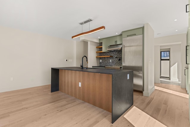 kitchen with a sink, under cabinet range hood, dark countertops, light wood finished floors, and green cabinetry