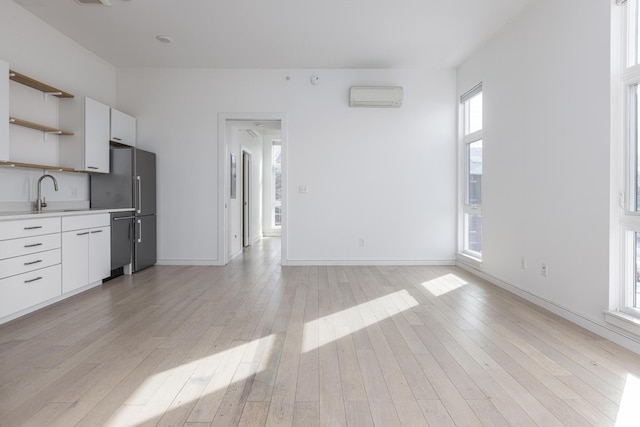 kitchen with an AC wall unit, appliances with stainless steel finishes, sink, white cabinets, and light hardwood / wood-style floors