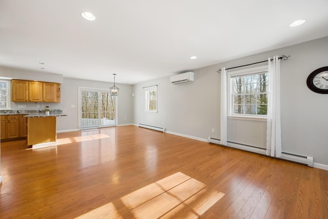 unfurnished living room with a baseboard heating unit, a wall unit AC, and light hardwood / wood-style floors