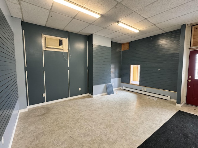 empty room featuring a wall unit AC, a paneled ceiling, and baseboard heating