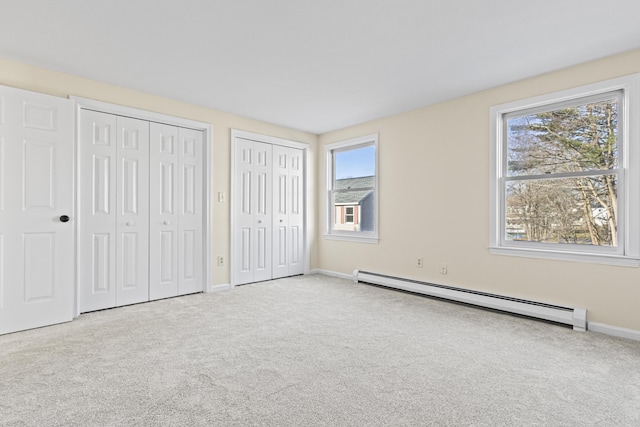 unfurnished bedroom with a baseboard radiator, light carpet, multiple windows, and two closets