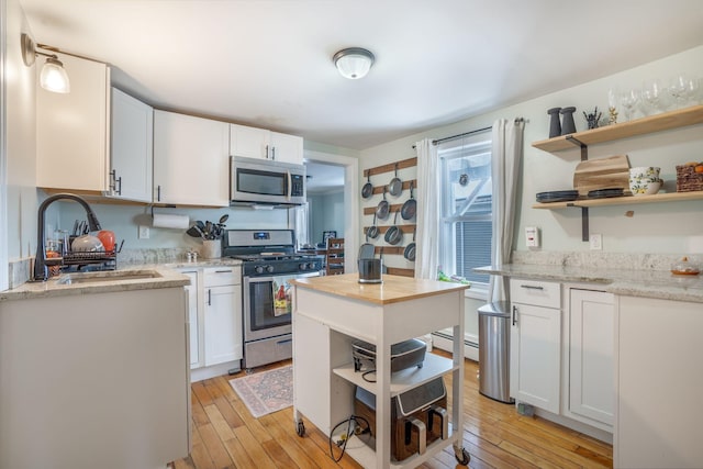 kitchen featuring sink, white cabinets, light stone counters, stainless steel appliances, and light hardwood / wood-style flooring