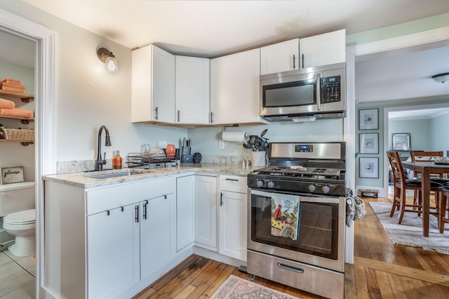 kitchen featuring sink, white cabinets, hardwood / wood-style flooring, light stone counters, and stainless steel appliances