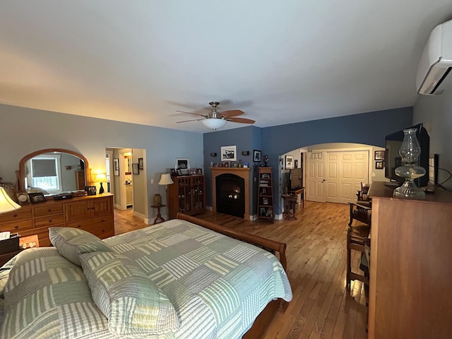 bedroom with ceiling fan, a wall mounted air conditioner, and light hardwood / wood-style floors