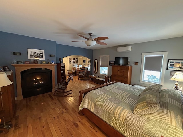 bedroom featuring hardwood / wood-style flooring, ceiling fan, an AC wall unit, and multiple windows