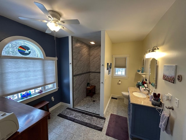 bathroom with vanity, ceiling fan, toilet, and a tile shower