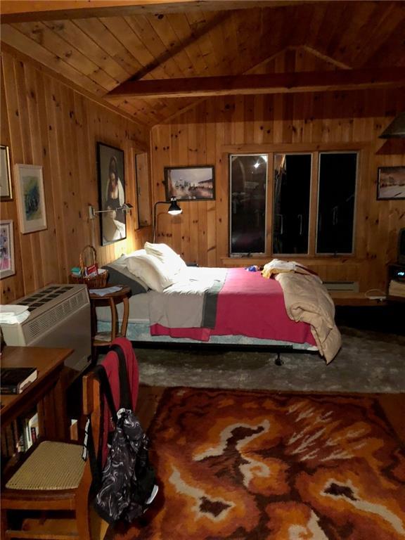 bedroom with vaulted ceiling, a wall mounted AC, wooden ceiling, and wooden walls