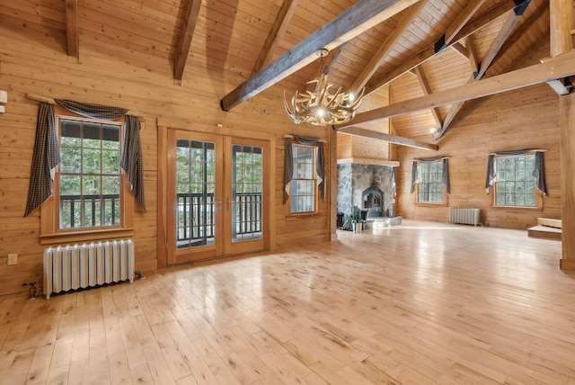 unfurnished living room with a notable chandelier, radiator heating unit, wooden walls, and french doors