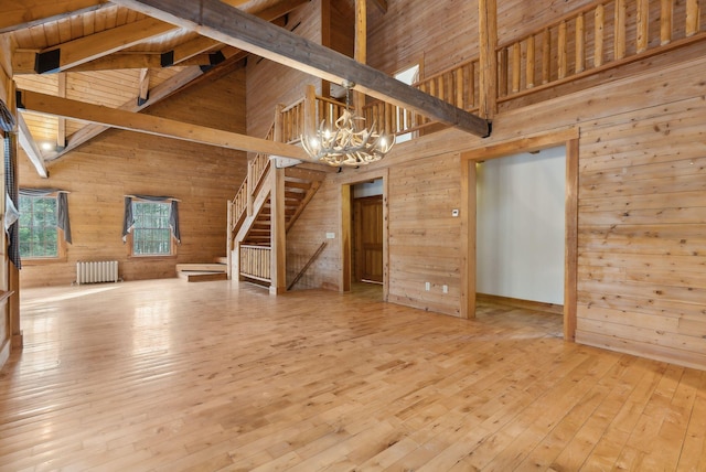 unfurnished living room with radiator, a notable chandelier, wooden walls, and light hardwood / wood-style floors