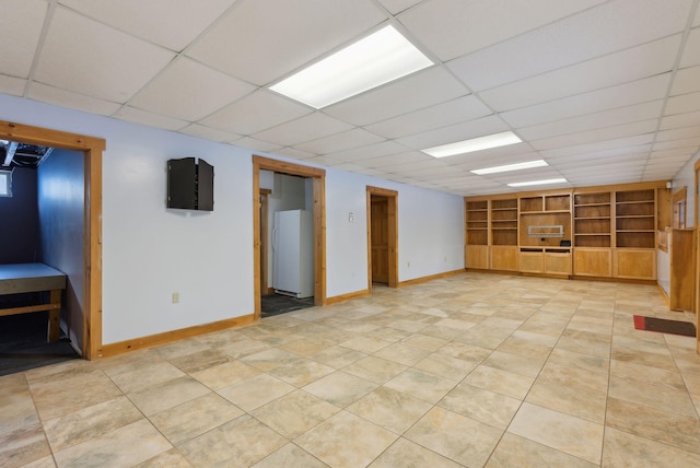 basement featuring light tile patterned flooring, white fridge, and a drop ceiling