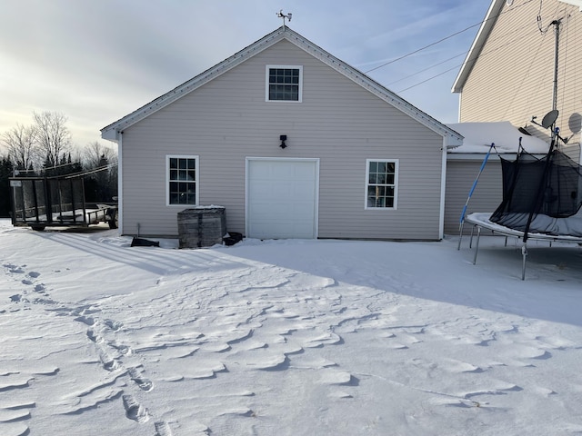 snow covered house with a garage and a trampoline