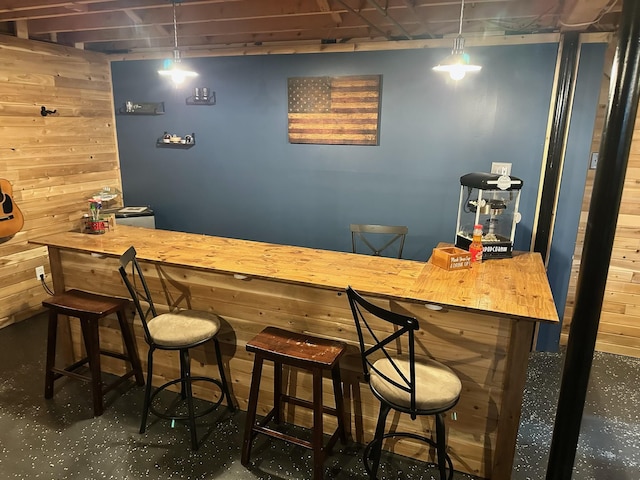 bar featuring wooden counters, hanging light fixtures, and wood walls