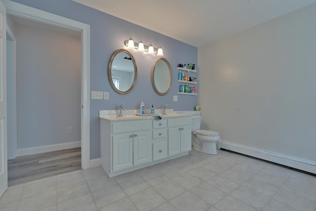 bathroom with a baseboard radiator, double vanity, toilet, a sink, and baseboards