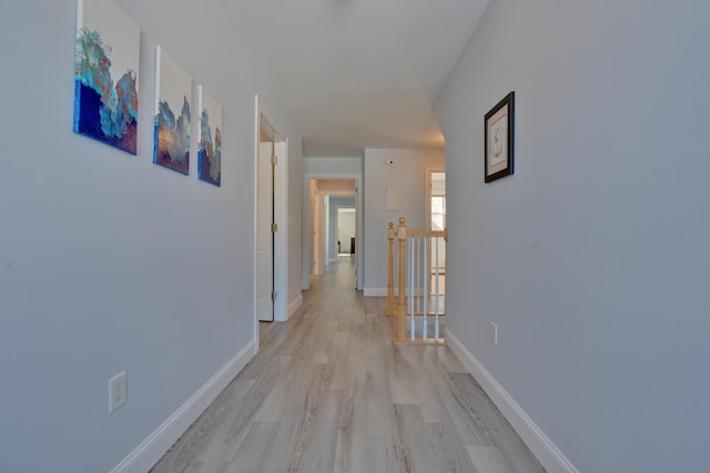 hallway with an upstairs landing, baseboards, and light wood-style floors