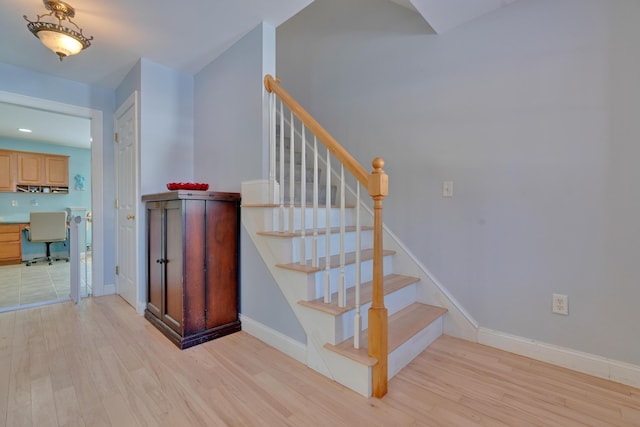 staircase featuring wood finished floors, built in desk, and baseboards