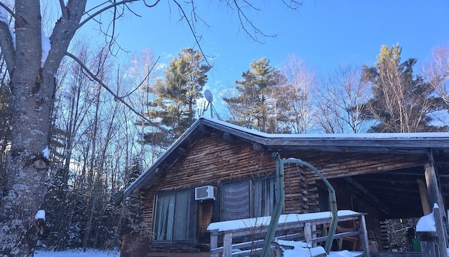 snow covered property with log exterior and a wall mounted air conditioner