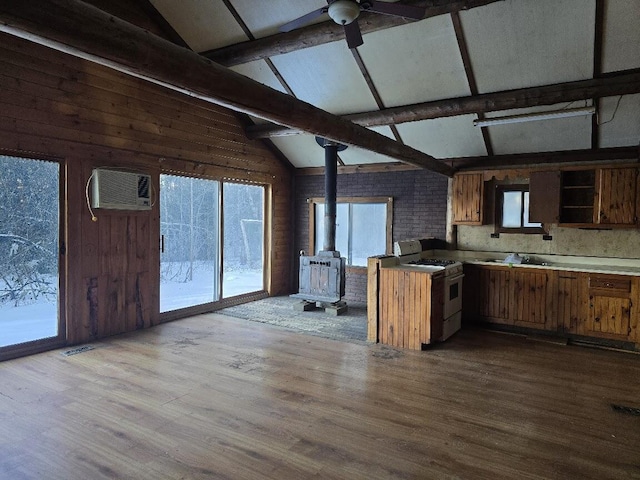 kitchen with brown cabinets, lofted ceiling with beams, gas range gas stove, a wall unit AC, and a wood stove