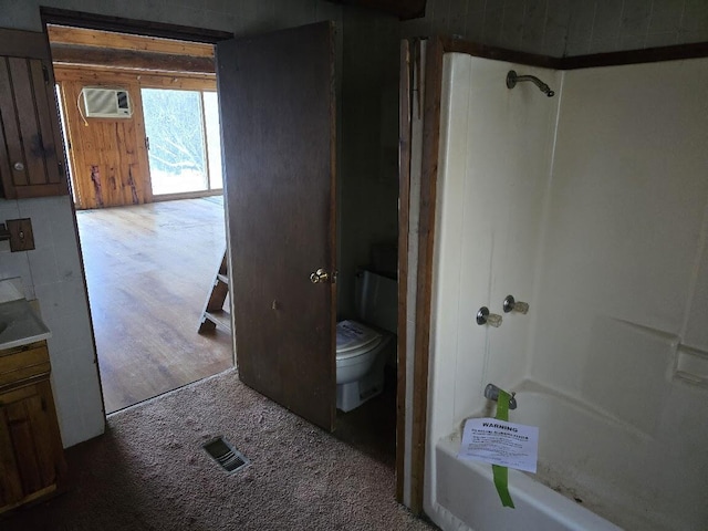 bathroom featuring toilet, an AC wall unit, wood finished floors, tub / shower combination, and vanity