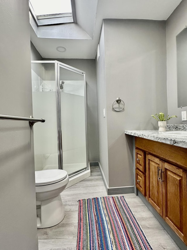 bathroom with a skylight, wood-type flooring, vanity, walk in shower, and toilet