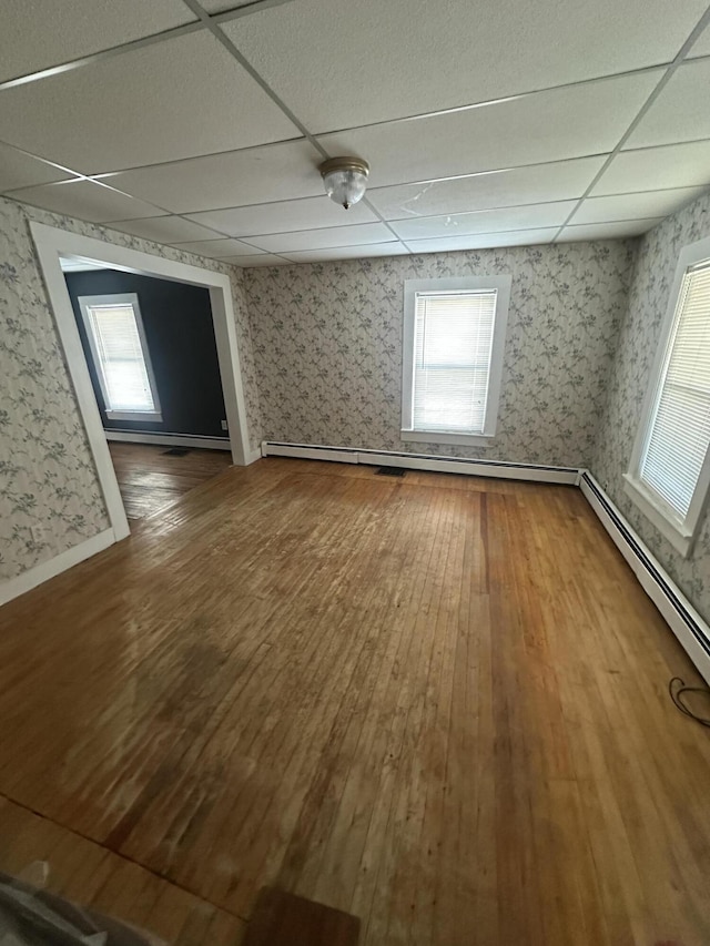 unfurnished room featuring a wealth of natural light, wood finished floors, a paneled ceiling, and wallpapered walls