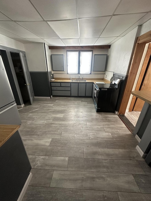 kitchen with a drop ceiling, gray cabinetry, a sink, electric stove, and light countertops