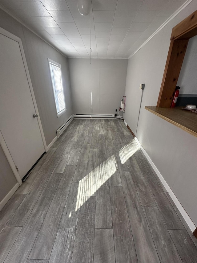 interior space featuring a baseboard heating unit, wood tiled floor, crown molding, and baseboards