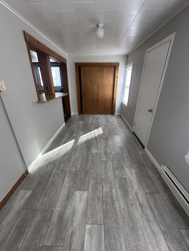 hallway featuring baseboard heating, wood finished floors, and baseboards